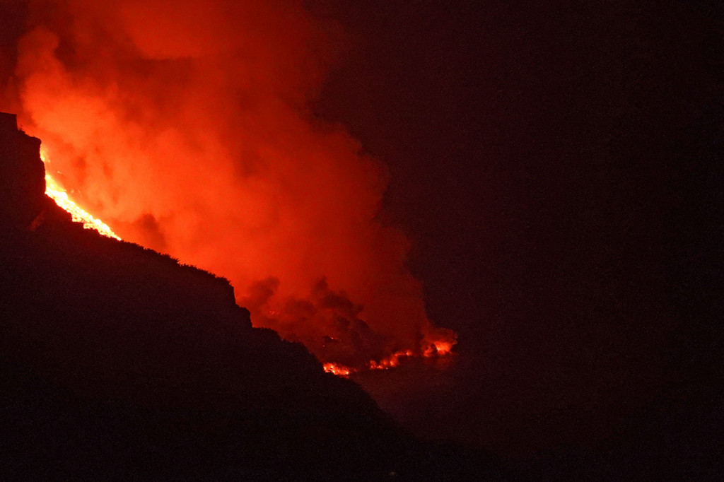 Lava merah panas dari gunung api Cumbre Vieja mengalir ke Samudra Atlantik pada Selasa, 28 September 2021, malam, sembilan hari setelah letusan pertama. Awan besar mengepul dari daerah Playa Nueva saat lava melakukan kontak dengan laut.