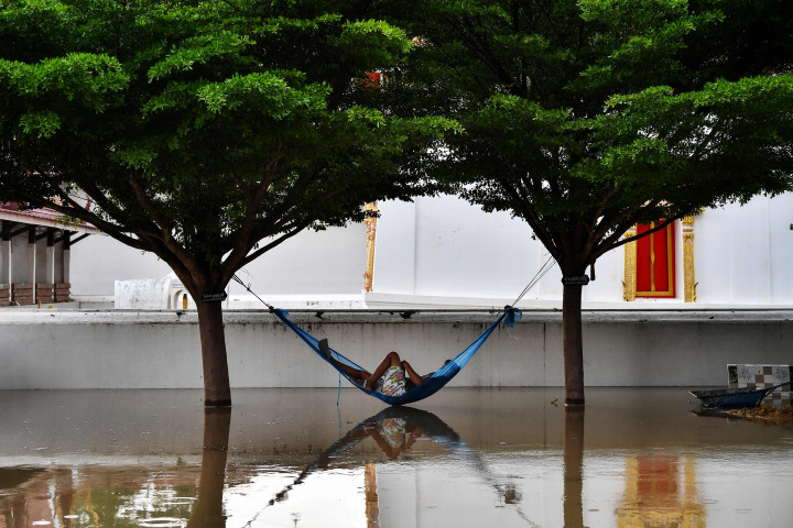 Seorang pria beristirahat di hammock di halaman kuil Buddha yang kebanjiran di Provinsi Ayutthaya, Thailand, Selasa, 28 September 2021.