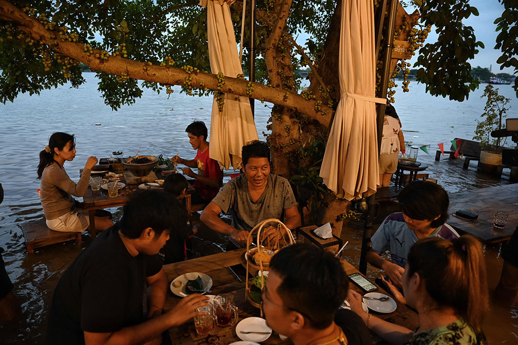 Pengunjung tengah menikmati sajian makanan di sebuah restoran yang tengah dilanda banjir di tepian sungai Chaopraya, Nonthaburi, Thailand, Kamis, 7 Oktober 2021.