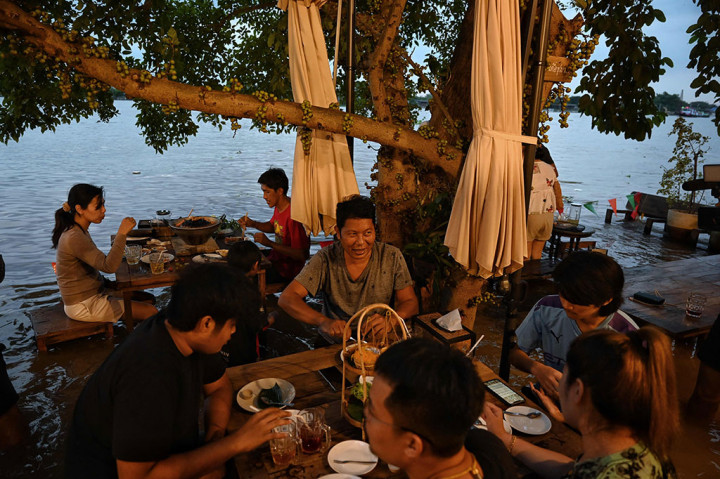 Pengunjung tengah menikmati sajian makanan di sebuah restoran yang tengah dilanda banjir di tepian sungai Chaopraya, Nonthaburi, Thailand, Kamis, 7 Oktober 2021.