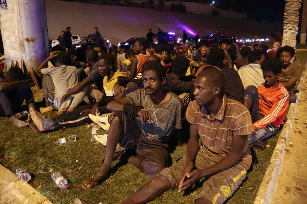Para imigran duduk di tanah setelah ditangkap kembali oleh pasukan keamanan Libya menyusul upaya melarikan diri dari fasilitas penahanan di Ibu Kota Libya, Tripoli, pada Jumat, 8 Oktober 2021 waktu setempat.