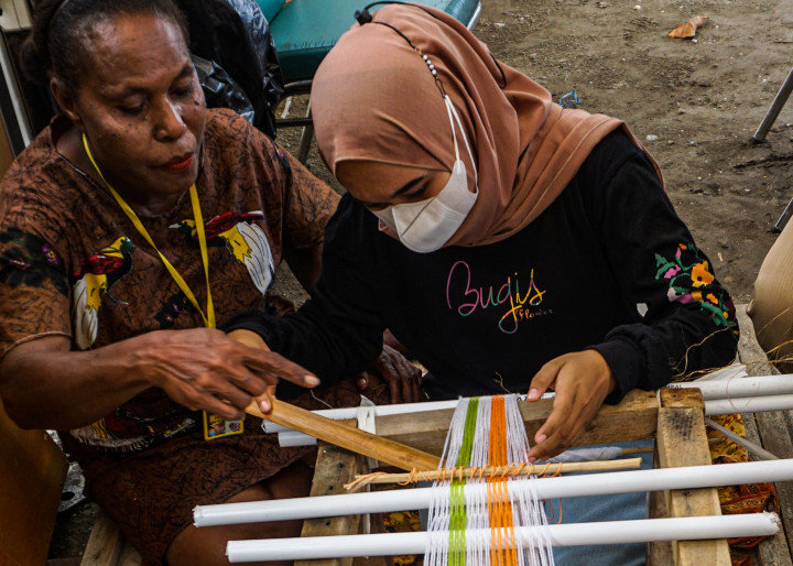 Penenun kain tervo Salonika Ambani (kiri) mengajarkan cara menenun kepada seorang wisatawan di sebuah stan Pameran dan Pagelaran Budaya Nasional di Holtekamp Jayapura, Papua, Kamis, 14 Oktober 2021.