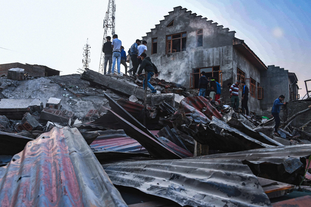 Warga berdiri di tengah puing-puing sebuah rumah yang rusak dalam baku tembak antara pemberontak dan pasukan keamanan pemerintah India di daerah Drangbal Pampore di distrik Pulwama, Kashmir selatan pada 16 Oktober 2021.