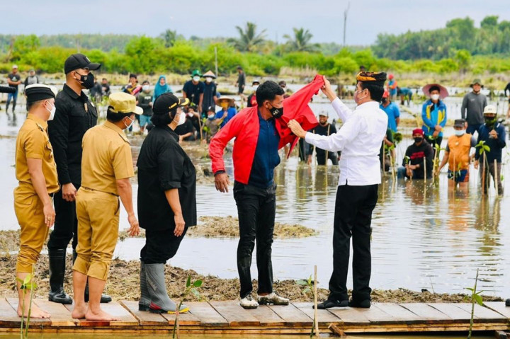 Presiden tampak memberikan jaket merahnya kepada seorang warga. 