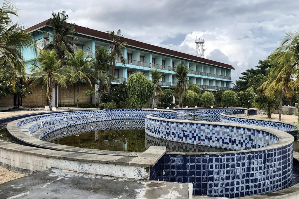 Kolam renang luas itu kini berisi air keruh dan berlumut. Hotel megah yang berdiri di depannya sama suramnya. Melompong.