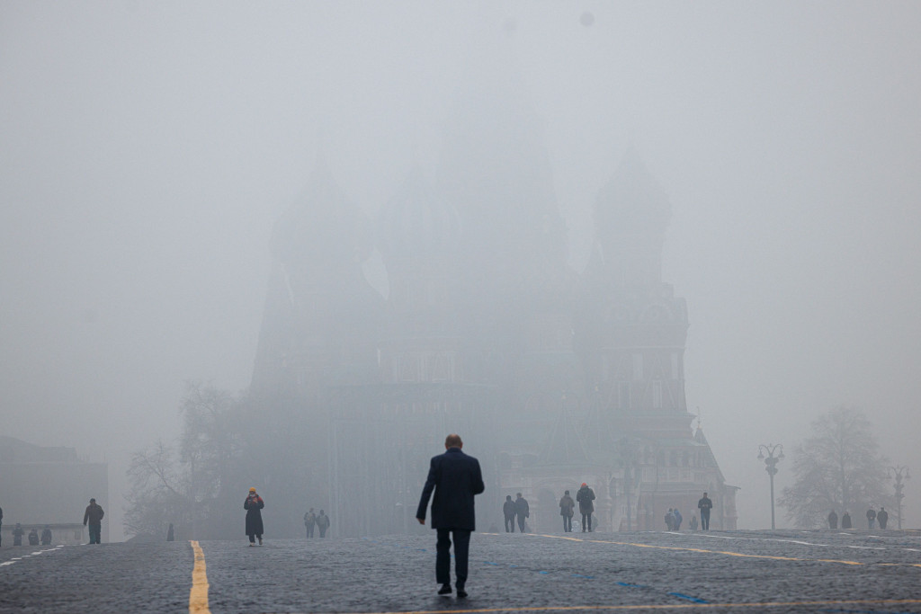 Orang-orang melintasi Lapangan Merah dengan Menara Spasskaya dan Katedral St. Basil yang tertutup kabut di pusat kota Moskow, Rusia.