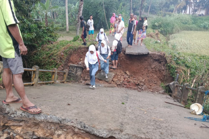 Siswa melewati jembatan Cikembang 2, Desa Karyamandala, Kecamatan Salopa, Kabupaten Tasikmalaya, yang amblas dan petugas BPBD mengevakuasi material longsor menimbun jalan tersebut, Selasa, 23 November 2021.