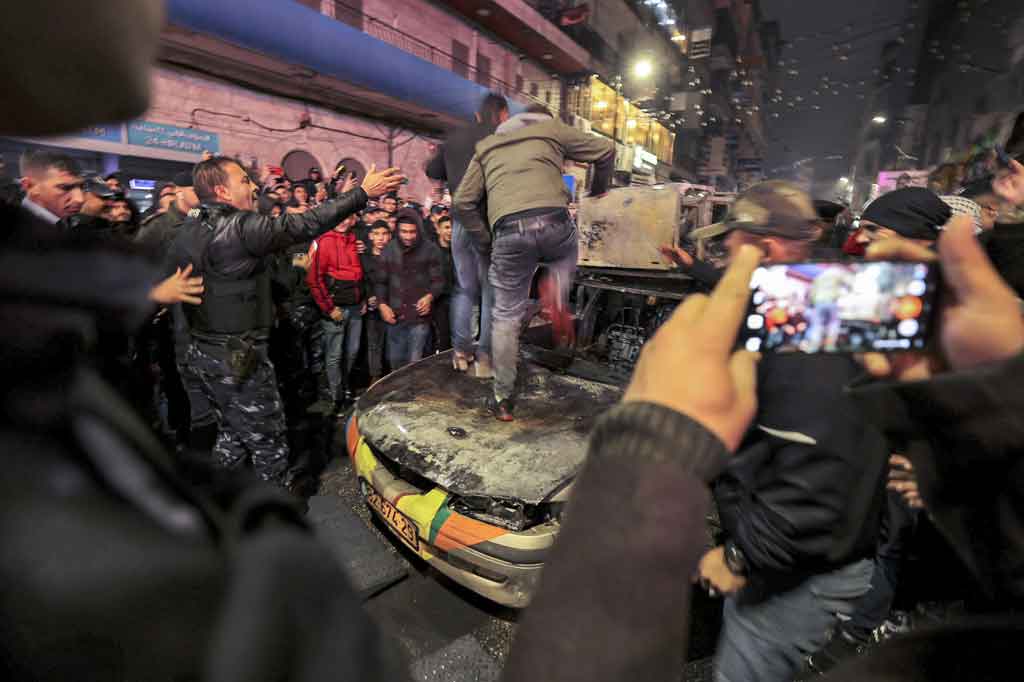 Seorang pemuda Palestina melompati kap mobil milik warga Israel yang dibakar di Kota Ramallah, Tepi Barat, 1 Desember 2021 malam waktu setempat.