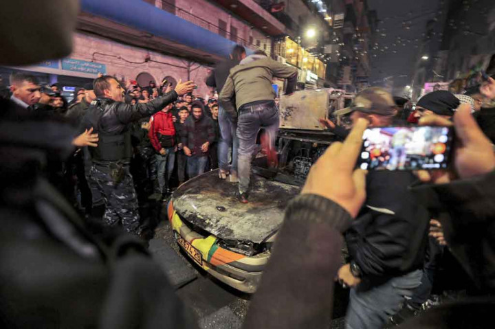 Seorang pemuda Palestina melompati kap mobil milik warga Israel yang dibakar di Kota Ramallah, Tepi Barat, 1 Desember 2021 malam waktu setempat.