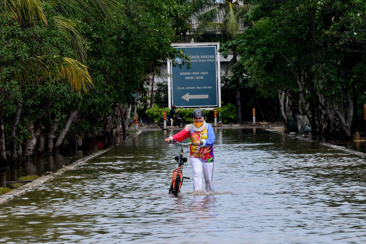 Pesepeda melintasi jalan yang tergenang akibat naiknya air laut ke permukaan (rob) di kawasan Pelabuhan Sunda Kelapa, Jakarta, Minggu, 5 Desember 2021.