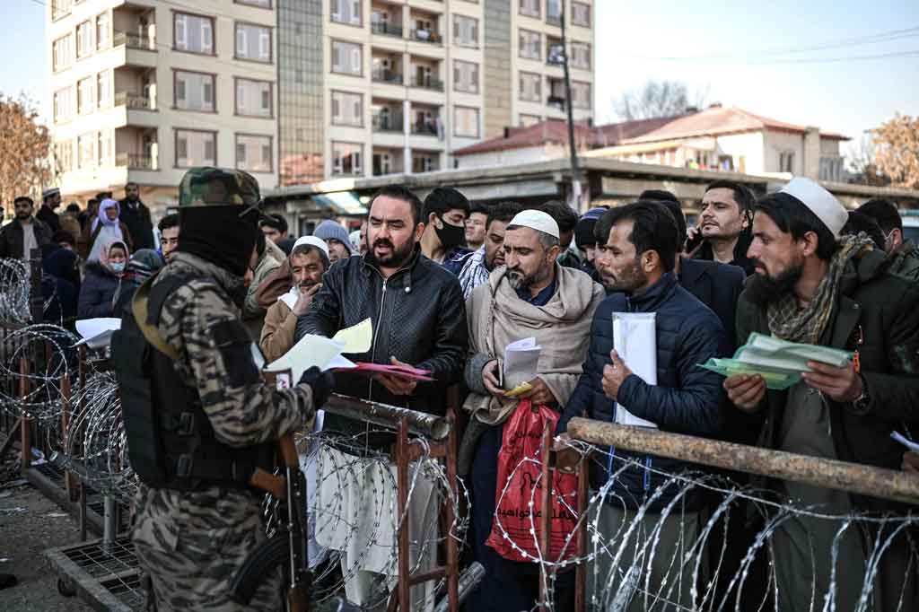 Seorang pejuang Taliban (kanan) memeriksa dokumen orang-orang yang mengantre untuk mengurus paspor di Kabul pada Sabtu, 18 Desember 2021. Otoritas Taliban Afghanistan mengatakan Sabtu, 18 Desember 2021, akan melanjutkan penerbitan paspor.