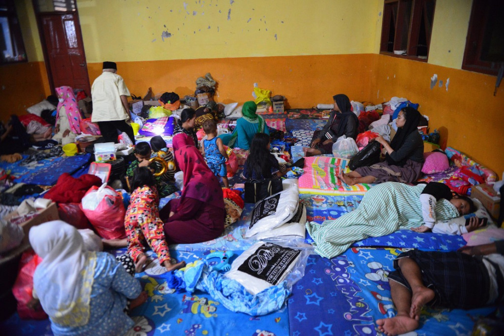 Petugas dan anak-anak sibuk mengangkut kantong berwarna oranye. Semua bergotong royong memindahkan bantuan dari sebuah truk yang terparkir tepat di gerbang SMPN 02 Pronojiwo, Lumajang, Jawa Timur, Minggu, 19 Desember 2021, malam. Dalam dua pekan ini, gedung sekolah itu menjadi tempat pengungsian korban bencana alam erupsi Gunung Semeru.