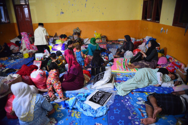 Petugas dan anak-anak sibuk mengangkut kantong berwarna oranye. Semua bergotong royong memindahkan bantuan dari sebuah truk yang terparkir tepat di gerbang SMPN 02 Pronojiwo, Lumajang, Jawa Timur, Minggu, 19 Desember 2021, malam. Dalam dua pekan ini, gedung sekolah itu menjadi tempat pengungsian korban bencana alam erupsi Gunung Semeru.