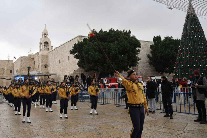 Di Manger Square Bethlehem, pengunjung dengan topi Santa dan pramuka menabuh genderang menandai Malam Natal pada hari Jumat, 24 Desember. Namun pengunjung lebih sedikit dari biasanya karena ketakutan terhadap virus corona membayangi perayaan untuk tahun kedua.