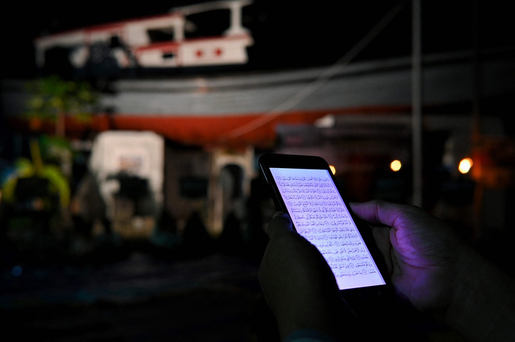 Seseorang membaca Al-Quran di ponselnya saat menghadiri doa bersama pada malam peringatan 17 tahun tsunami Boxing Day 2004 di monumen Kapal Tsunami Lampulo di Banda Aceh, 25 Desember 2021. 