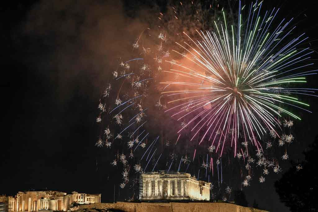 Kembang api menerangi langit di atas Acropolis Kuno di Athena, Yunani saat perayaan Malam Tahun Baru pada 31 Desember 2021. AFP PHOTO/Louisa Gouliamaki