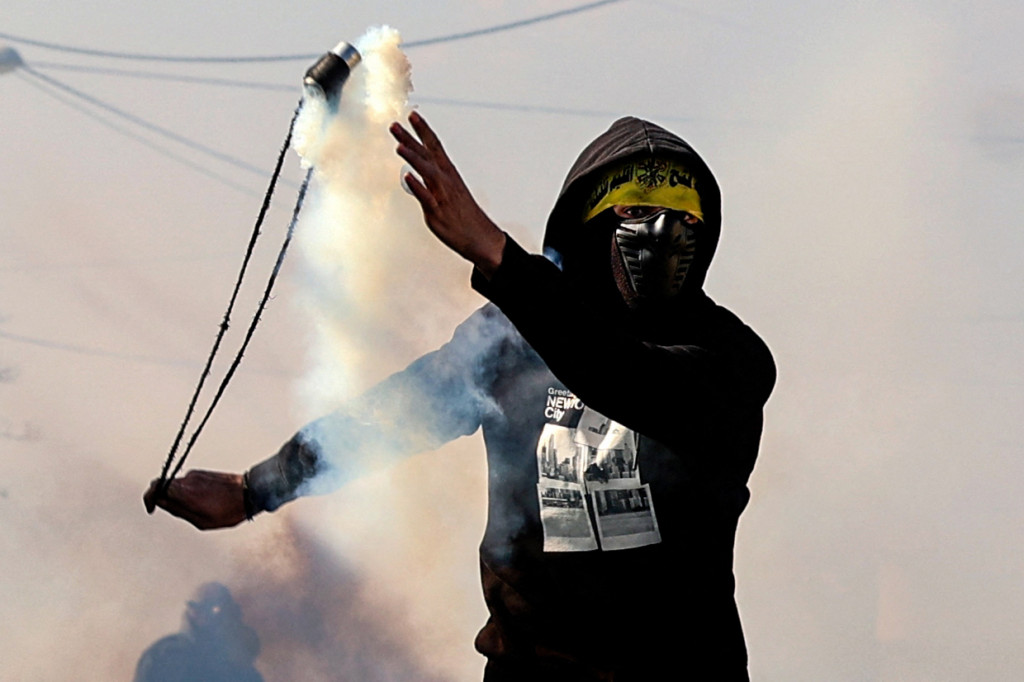 Seorang pemuda Palestina menggunakan ketapel untuk mengembalikan tabung gas air mata ke arah pasukan kemanan Israel saat bentrok pada demonstrasi menentang pengambilalihan tanah oleh Israel dekat permukiman Yahudi Kadumim di Desa Kfar Qaddum, Tepi Barat, 21 Januari 2022.