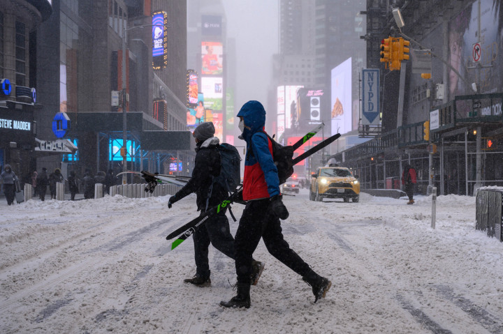 Orang-orang membawa alat ski saat mereka berjalan melewati salju di sepanjang jalan di New York pada 29 Januari 2022.