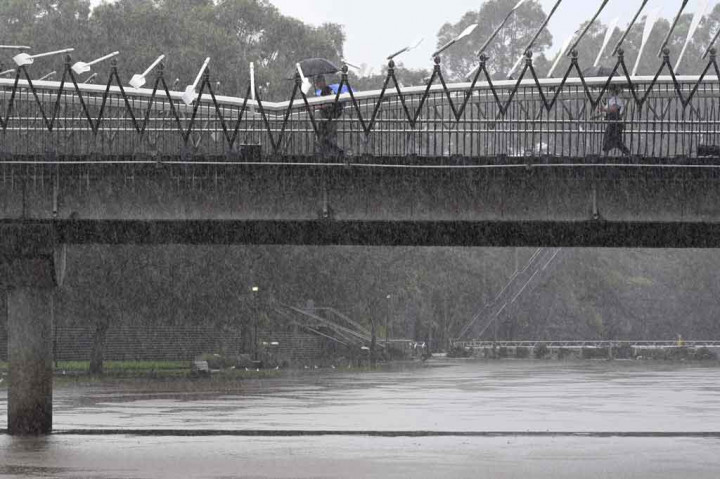 Pejalan kaki berjalan di jembatan di atas sungai Parramatta, Sydney, yang meluap pada Rabu, 23 Februari 2022. Hujan lebat mengguyur Australia timur, menyebabkan banjir bandang dan serangkaian peringatan darurat di sepanjang pantai Pasifik.