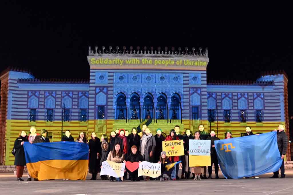 Sekelompok kecil warga berkumpul di depan balai kota Sarajevo yang diterangi warna-warni bendera Ukraina, pada 24 Februari 2022. AFP PHOTO/Elvis Barukcic