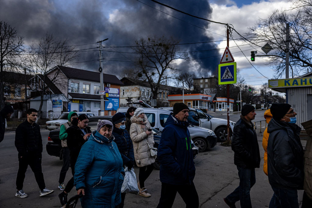 Orang-orang mengantre di depan supermarket sementara asap mengepul di atas kota Vasylkiv di luar Kiev, 27 Februari 2022.