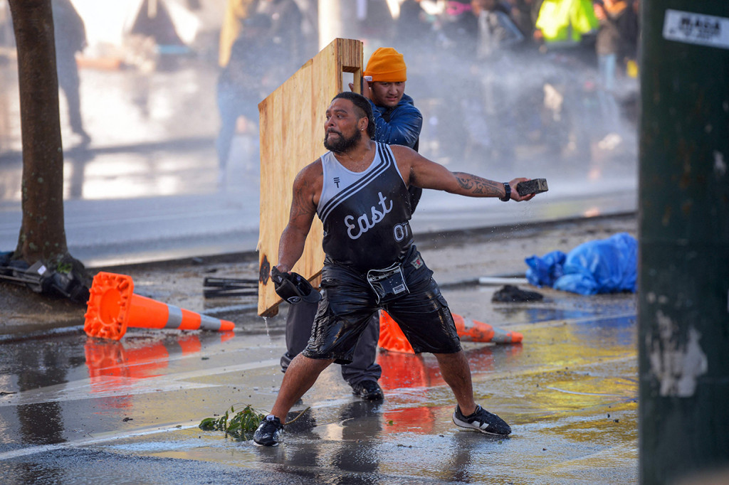 Seorang pengunjuk rasa akan melempar batu saat melakukan perlawanan terhadap polisi di depan Parlemen di Wellington, Selandia Baru, Rabu, 2 Maret 2022.