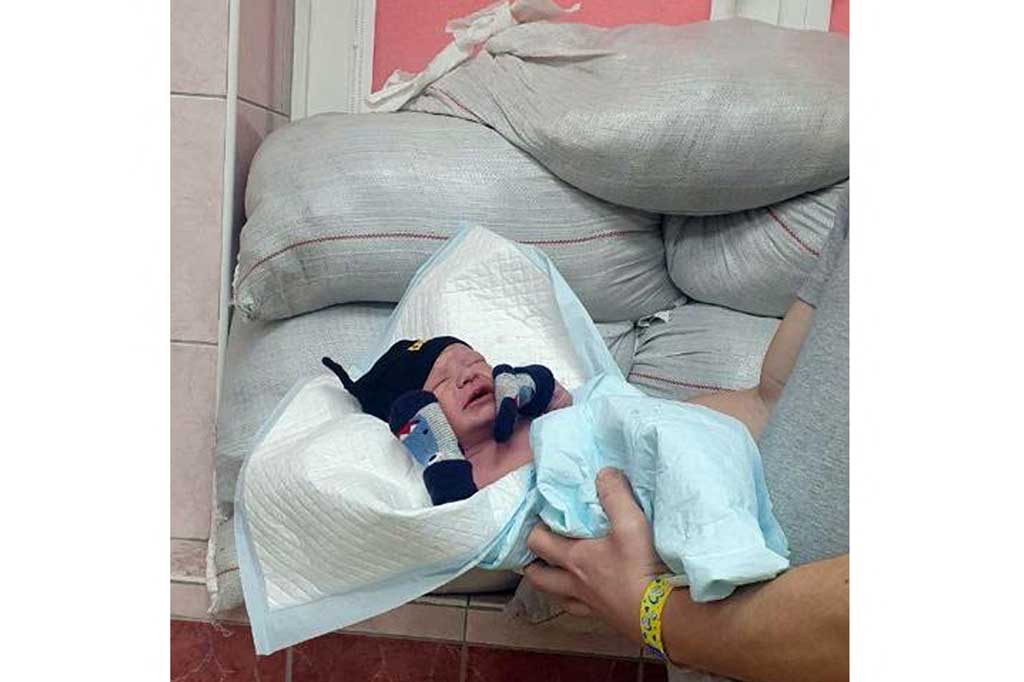 Bayi yang baru lahir berpose terlihat di depan jendela yang dilindungi  karung berisi pasir di Rumah Sakit Bersalin Kyiv No. 6 pada awal Maret 2022, saat ibu kota Ukraina menghadapi serangan pasukan Rusia.