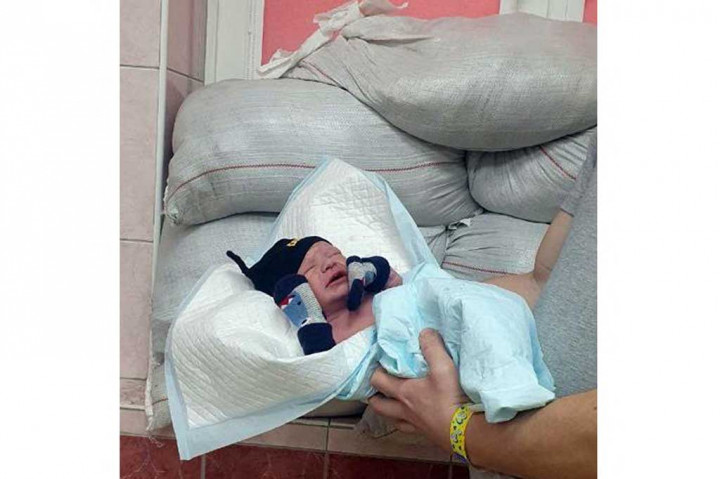 Bayi yang baru lahir berpose terlihat di depan jendela yang dilindungi  karung berisi pasir di Rumah Sakit Bersalin Kyiv No. 6 pada awal Maret 2022, saat ibu kota Ukraina menghadapi serangan pasukan Rusia.