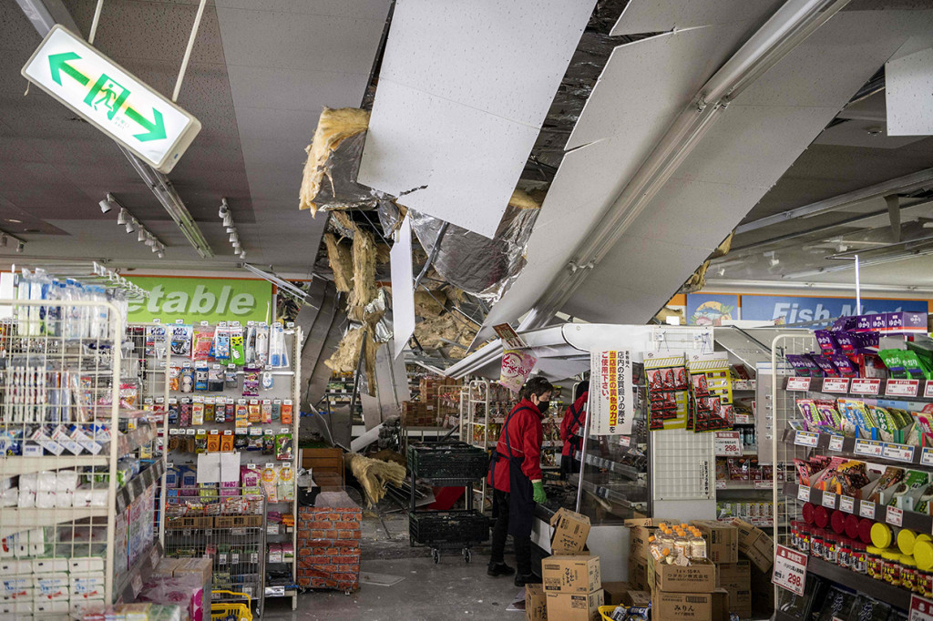 Karyawan mengeluarkan barang dagangan dari rak di bawah langit-langit yang rusak di sebuah supermarket di Shiroishi, prefektur Miyagi pada 17 Maret 2022 setelah gempa Magnitudo 7,3 mengguncang Jepang timur malam sebelumnya.