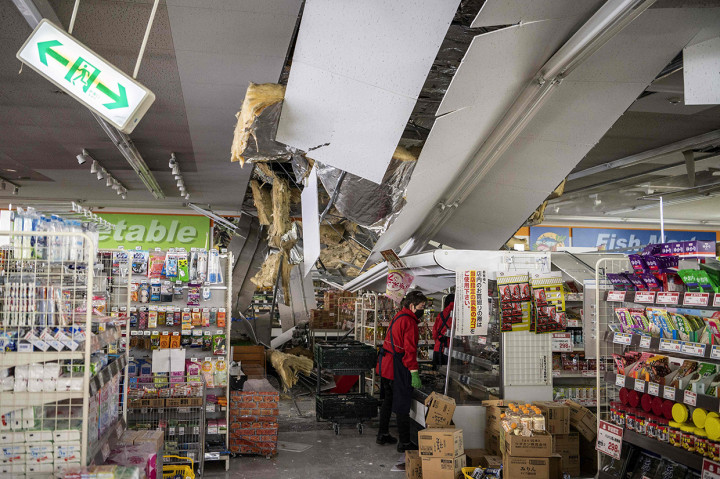 Karyawan mengeluarkan barang dagangan dari rak di bawah langit-langit yang rusak di sebuah supermarket di Shiroishi, prefektur Miyagi pada 17 Maret 2022 setelah gempa Magnitudo 7,3 mengguncang Jepang timur malam sebelumnya.