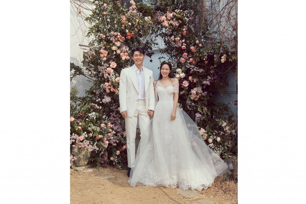 Agensi Hyun Bin, VAST Entertainment membagikan foto pernikahan pasangan drama Korea Crash Landing On You itu. Dalam foto pertama, Hyun Bin dan Son Ye Jin terlihat serasi memakai busana pengantin bernuasa putih. Son Ye Jin tampak semringah saat tangannya digandeng Hyun Bin di bawah dekorasi karangan bunga berwarna pink dan ungu di sebuah taman.