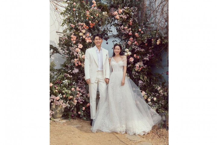 Agensi Hyun Bin, VAST Entertainment membagikan foto pernikahan pasangan drama Korea Crash Landing On You itu. Dalam foto pertama, Hyun Bin dan Son Ye Jin terlihat serasi memakai busana pengantin bernuasa putih. Son Ye Jin tampak semringah saat tangannya digandeng Hyun Bin di bawah dekorasi karangan bunga berwarna pink dan ungu di sebuah taman.