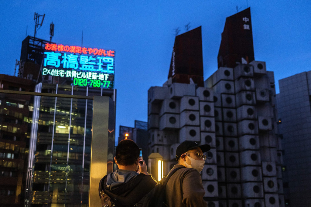 Orang-orang memotret Nakagin Capsule Tower (kanan), sebuah bangunan perumahan perkantoran serba guna di distrik Ginza Tokyo, 6 April 2022.
