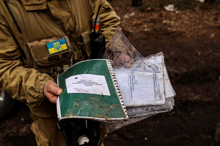 Seorang anggota tentara Ukraina menunjukkan buku catatan Rusia yang ditemukan di kamp pangkalan Rusia yang kosong di dekat Buda-Babynetska, utara Kiev, pada 5 April 2022.