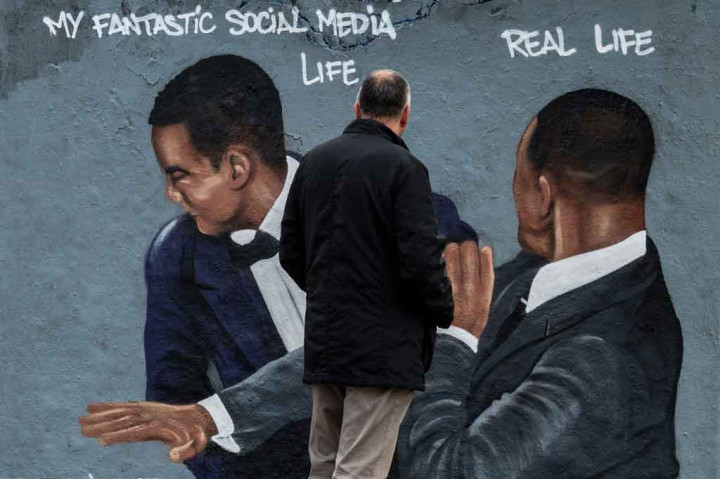 Seorang pria melihat lukisan dinding karya seniman jalanan yang berbasis di Berlin, Eme Freethinker, yang menampilkan aktor AS Will Smith (kanan) menampar komedian AS Chris Rock selama upacara Oscar, di Berlin pada 30 Maret 2022 lalu.