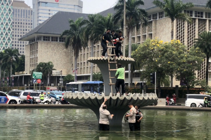 Sebanyak tiga orang polisi bersiaga di bawah. Sedangkan dua polisi lainnya dan petugas Dinas Kehutanan merangkul dan memeluk pemuda itu agar tidak jatuh.