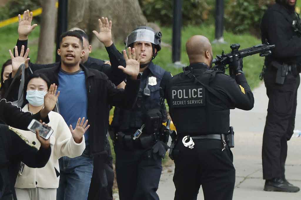 Polisi terlihat menodongkan senjata ke atas di sebuah gedung apartemen saat mereka mengawal warga sipil dari tempat kejadian, sementara sejumlah ambulans juga ada di lokasi.