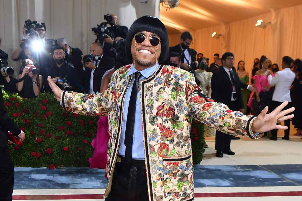 Anderson Paak mengenakan jas berwarna kuning dengan motif floral berpadu kemeja biru muda, dasi hitam, celana panjang hitam model cutbray dan kacamata hitam. Sang penyanyi melengkapi penampilannya dengan model rambut berponi.