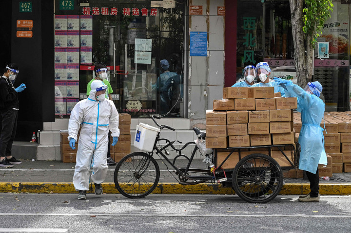 Pekerja mengenakan alat pelindung diri menumpuk kotak ke atas gerobak untuk dikirim saat pemberlakuan lockdown karena virus Covid-19 di Distrik Jing'an, Shanghai, Tiongkok, Rabu, 18 Mei 2022.