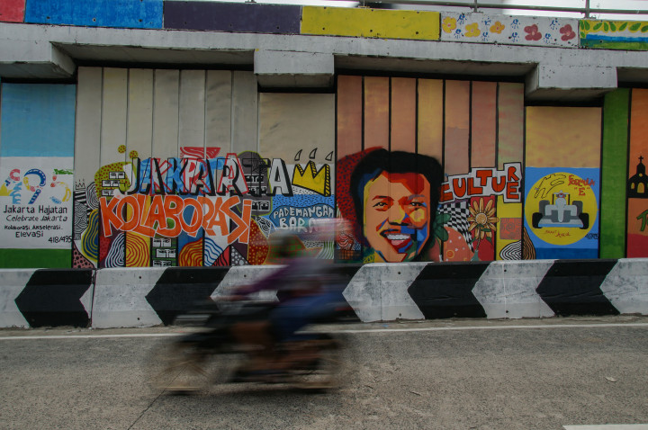 Pengendara melintas di depan mural bertema HUT ke-495 DKI di kawasan Ancol, Jakarta, Senin, 6 Juni 2022. 