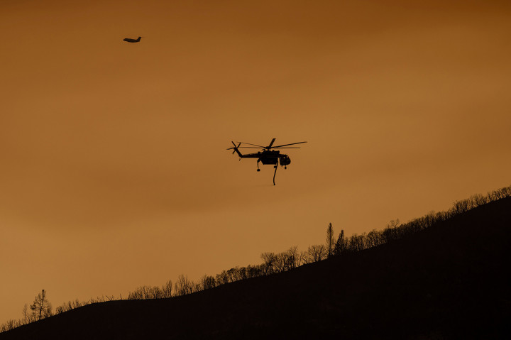 Sebuah pesawat pemadam kebakaran terbang melalui langit yang dipenuhi asap di dekat punggung bukit yang terbakar di Oak Fire dekat Mariposa, California, pada 24 Juli 2022.