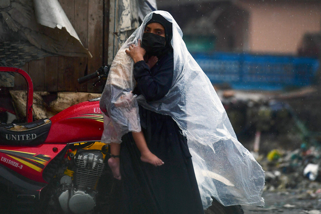 Seorang wanita menggunakan plastik untuk melindungi putrinya dari rintik hujan yang terus turun.