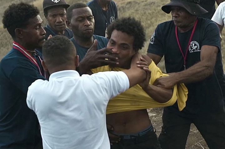 Petugas keamanan menahan seorang pria (berbaju kuning) yang menyerang seorang pelaut Jepang dengan gunting selama upacara peringatan Perang Dunia II untuk menandai peringatan ke-80 Pertempuran Guadalcanal, di Honiara, Kepulauan Solomon pada Senin, 8 Agustus 2022.