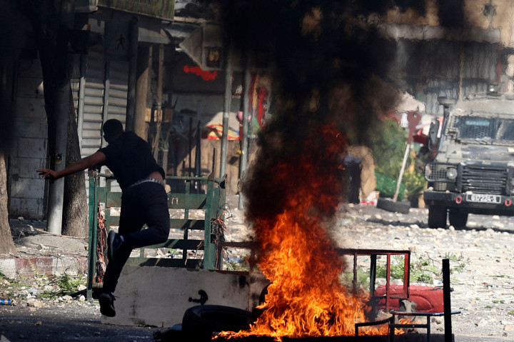 Pengunjuk rasa Palestina melemparkan batu ke kendaraan pasukan keamanan Israel selama serangan di kota tua Nablus, di Tepi Barat yang diduduki, pada 9 Agustus 2022.