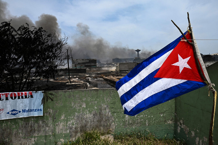 Sebuah bendera Kuba berkibar di dekat area yang hancur akibat kebakaran dahsyat pada tangki minyak di dekat pelabuhan di Matanzas.