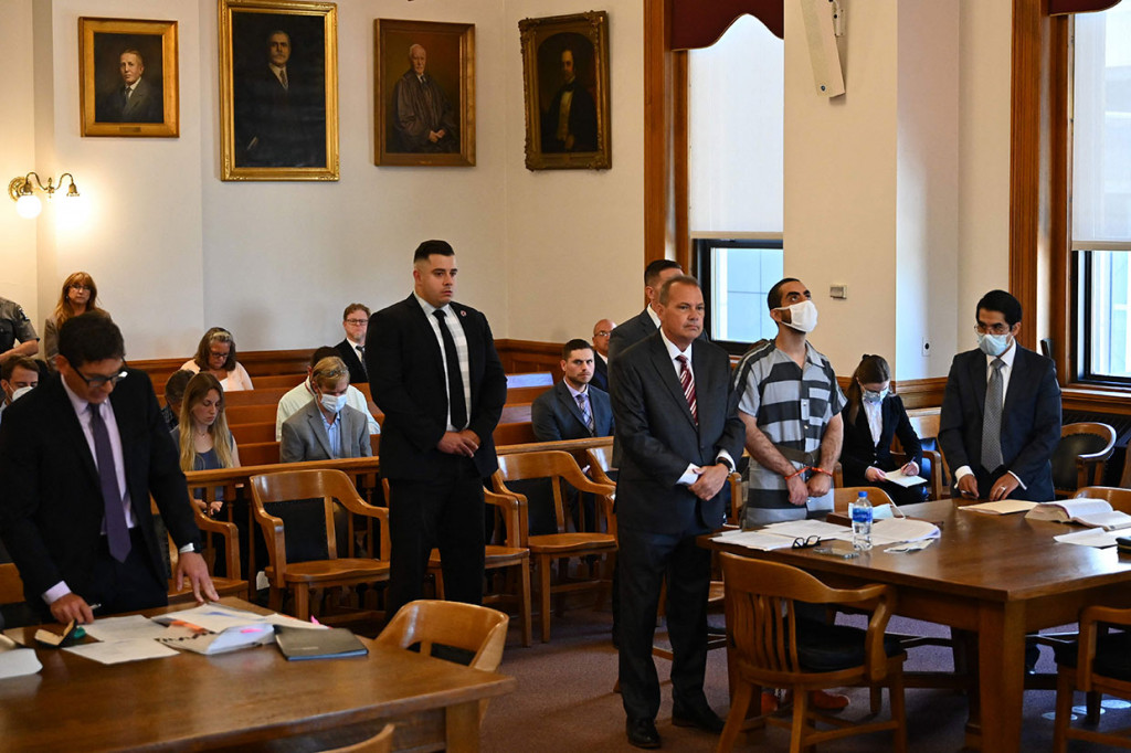 Diborgol dan mengenakan pakaian penjara bergaris hitam dan putih, Hadi Matar, 24, menjawab dakwaan juri setelah dia diduga menyerbu panggung pada acara Jumat, 12 Agustus lalu, dan menikam Rushdie berulang kali di leher dan perut. Rusdhie dalam kondisi kritis akibat penikaman tersebut.