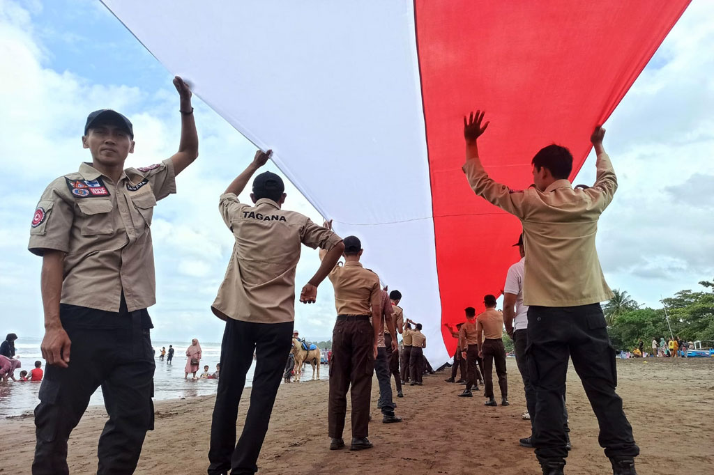 Ribuan warga Pangandaran, Jawa Barat membentangkan bendera merah putih raksasa sepanjang 1 Km di Pantai Pangandaran, Kamis, 18 Agustus 2022. Kegiatan tersebut untuk menumbuhkan semangat nasionalisme bertepatan dengan HUT ke-77 Kemerdekaan RI.