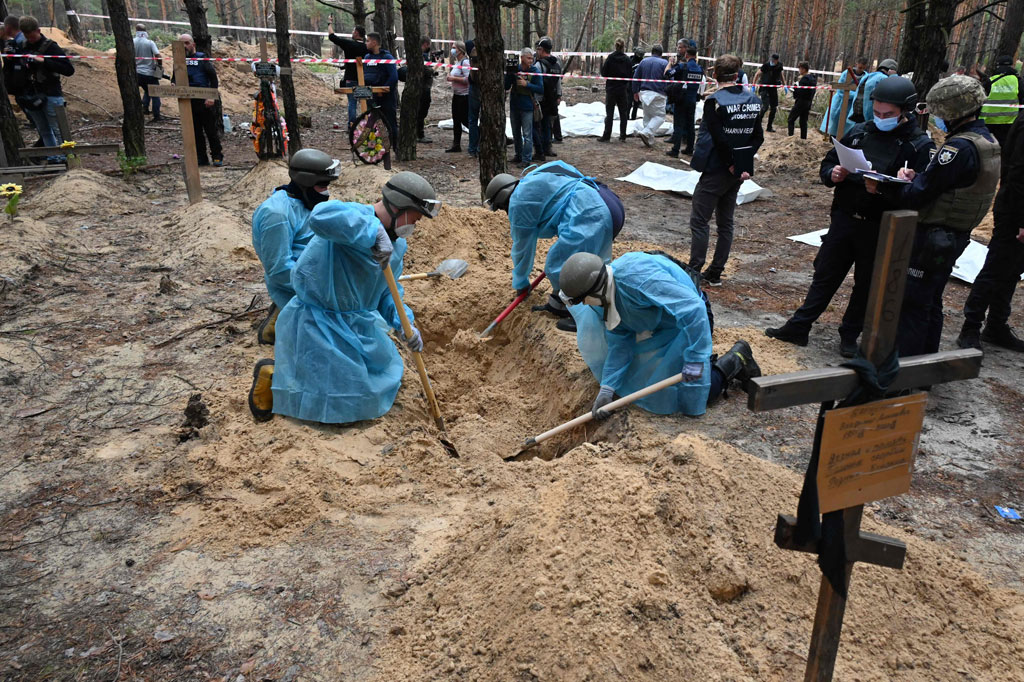 Penyelidik Ukraina turun ke hutan pinus di luar kota Izium yang direbut kembali dari Rusia pada hari Jumat, 16 September 2022, dan mulai menggali serta menarik ratusan jenazah yang terkubur dengan tergesa-gesa dari tanah berpasir. 
