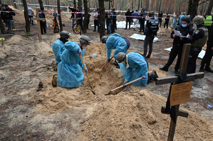 Penyelidik Ukraina turun ke hutan pinus di luar kota Izium yang direbut kembali dari Rusia pada hari Jumat, 16 September 2022, dan mulai menggali serta menarik ratusan jenazah yang terkubur dengan tergesa-gesa dari tanah berpasir. 