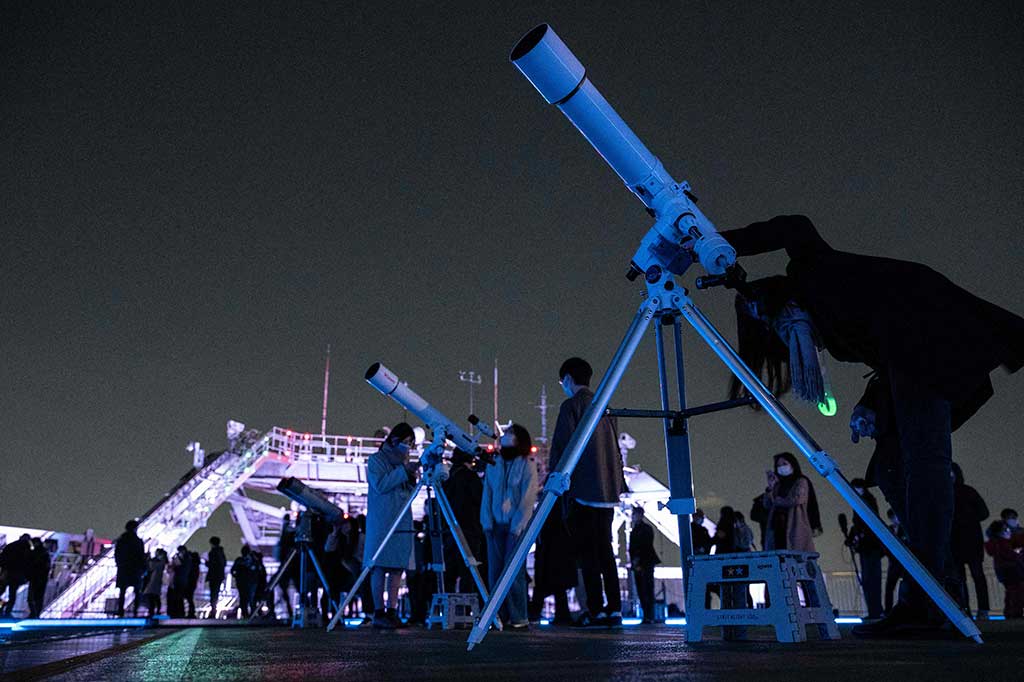Awak media dan masyarakat umum melihat gerhana bulan total dengan teleskop dan mata telanjang di atas langit Tokyo dari atap gedung tinggi, pada Selasa, 8 November 2022. AFP PHOTO/Richard A. Brooks